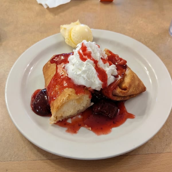 Golden-fried dessert chimichanga topped with whipped cream, strawberry sauce, and a scoop of vanilla ice cream.