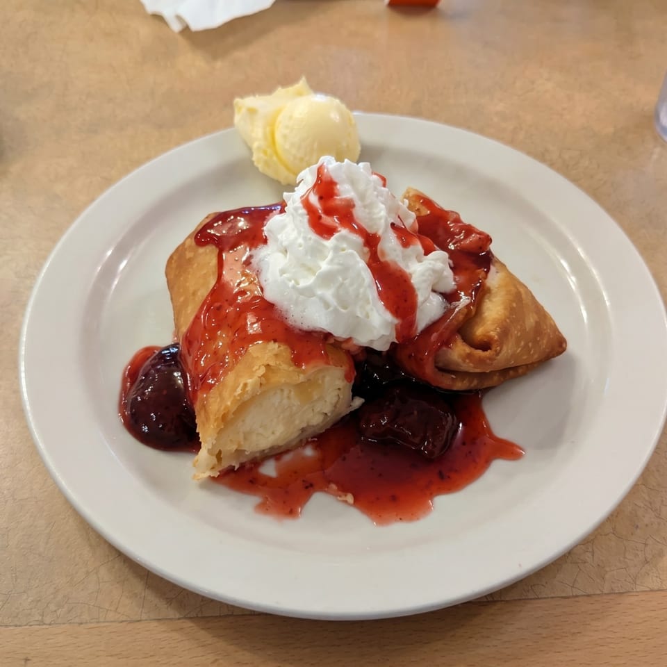Golden-fried dessert chimichanga topped with whipped cream, strawberry sauce, and a scoop of vanilla ice cream.