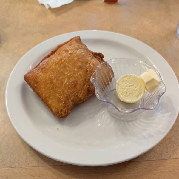 A golden-brown fried pastry with a side of butter in a clear dish on a white plate.