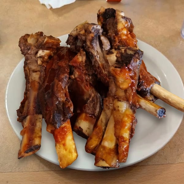 A white plate piled high with several large, saucy barbecue ribs on a wooden table.