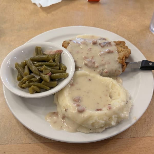 Chicken fried steak with gravy, mashed potatoes, and a side of green beans on a white plate.
