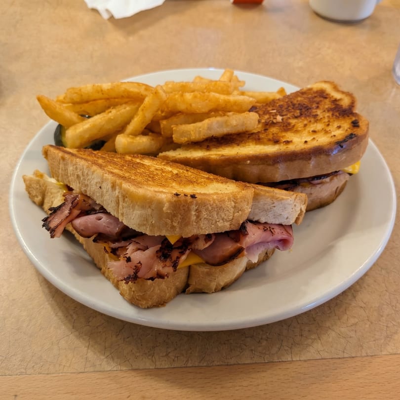 Grilled ham and cheese sandwich with crispy bacon and a side of golden french fries.