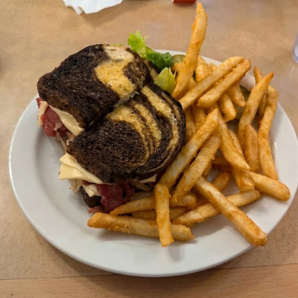 Marble rye Reuben sandwich with corned beef, Swiss cheese, sauerkraut, and a side of french fries.