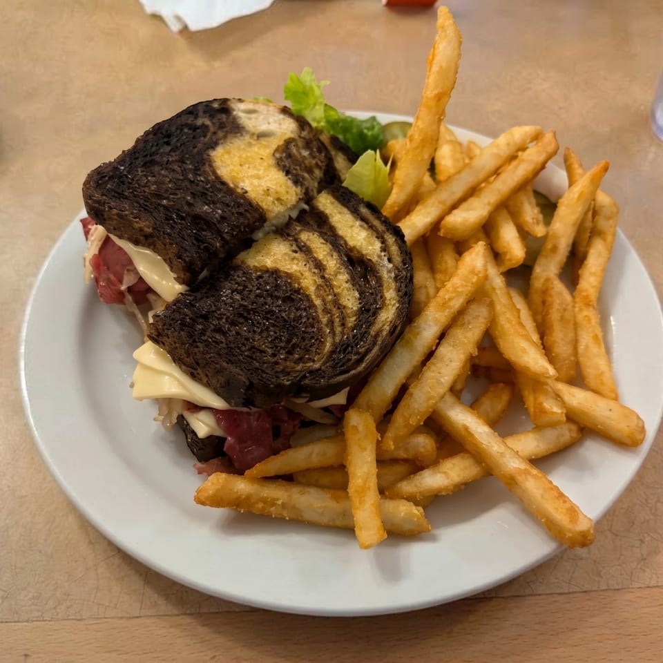 Marble rye Reuben sandwich with corned beef, Swiss cheese, sauerkraut, and a side of french fries.
