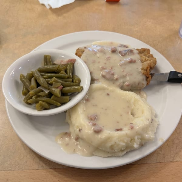 Chicken fried steak with gravy, mashed potatoes, and a side of green beans on a white plate.