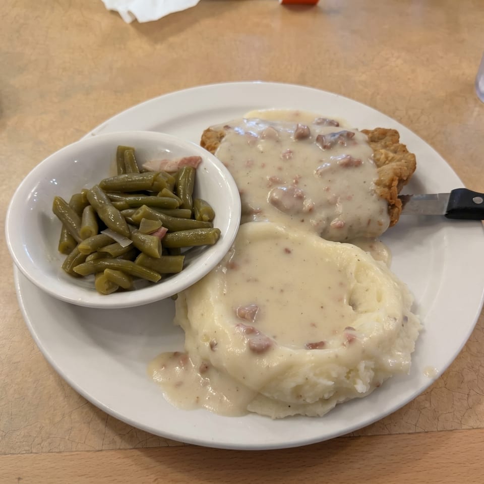 Chicken fried steak with gravy, mashed potatoes, and a side of green beans on a white plate.