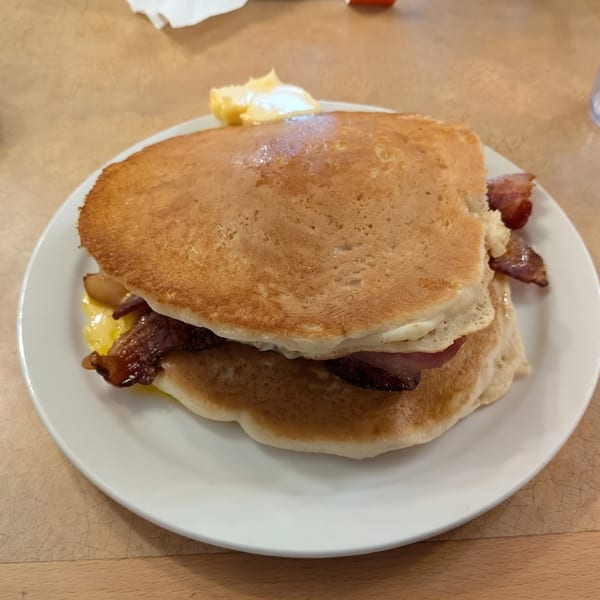 A stack of pancakes with bacon, scrambled eggs, and a pat of butter on a white plate.